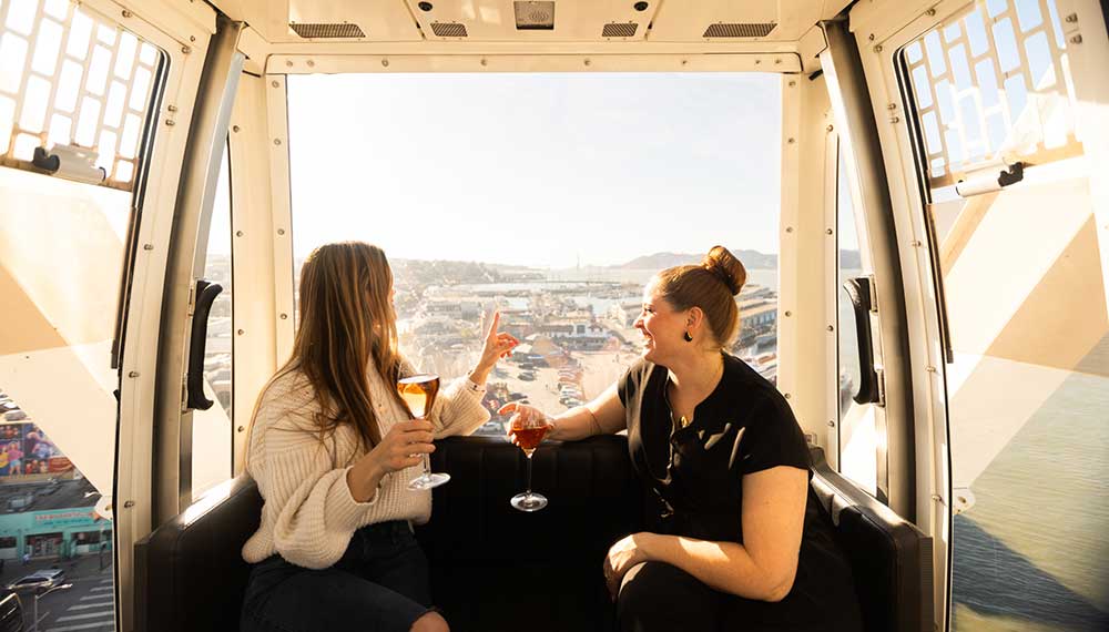 two women with glasses of wine in some sort of gondola above the city
