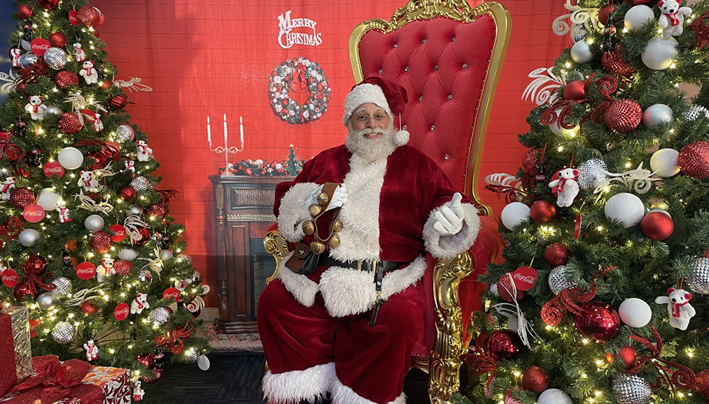 Santa Claus sitting in a red chair flanked by christmas trees
